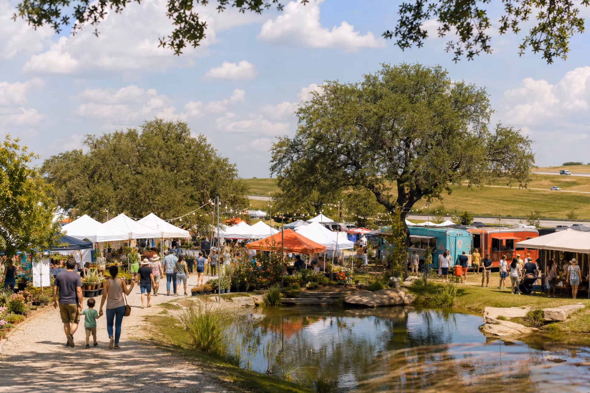 Mines Market vendor tents and food trucks beside the pond under a Hill Country sky